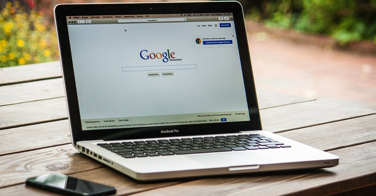 MacBook Pro on a wooden table showing the Google homepage